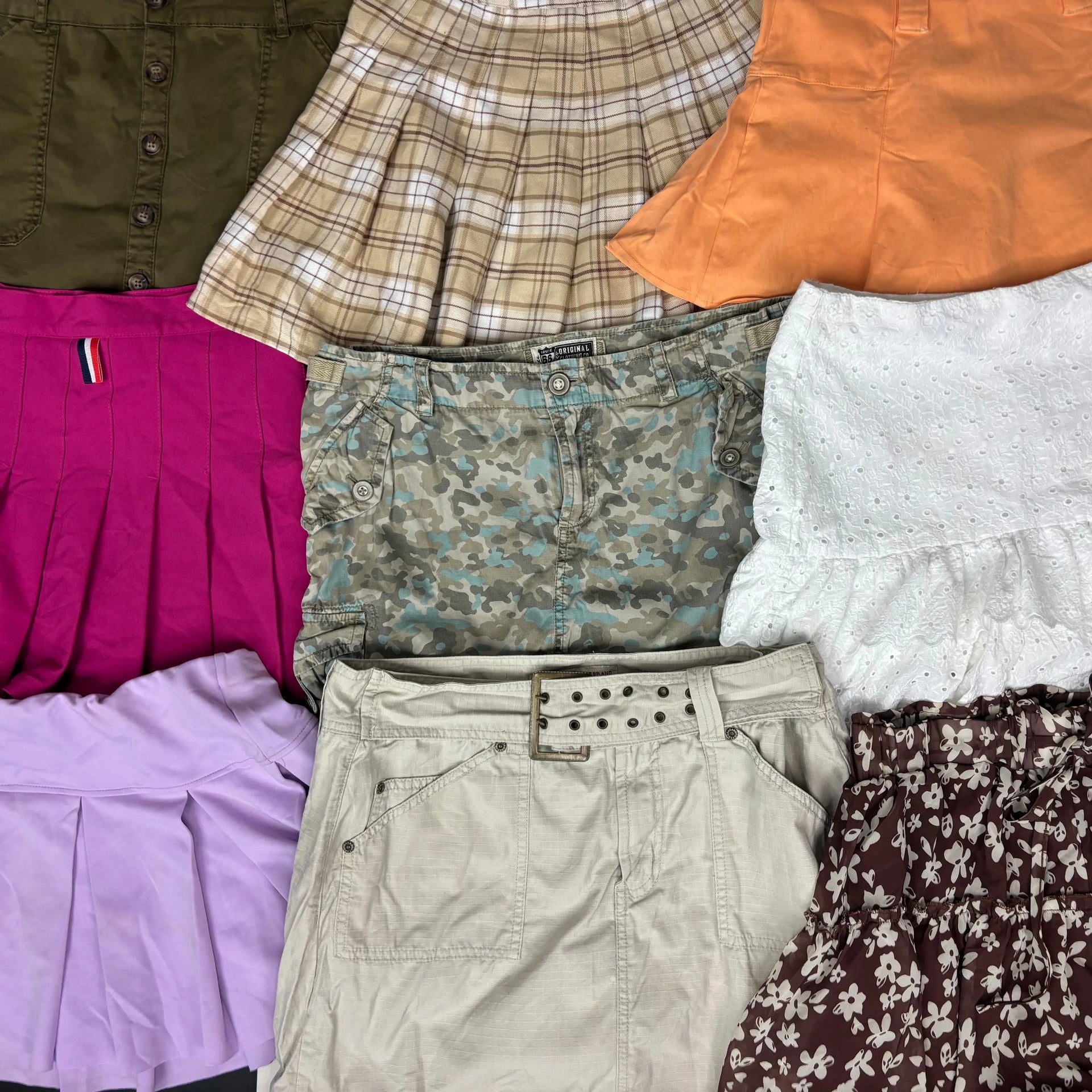 Assortment of 10 colorful mini skirts including plaid, floral, solid pleated, and belted styles in spring shades.