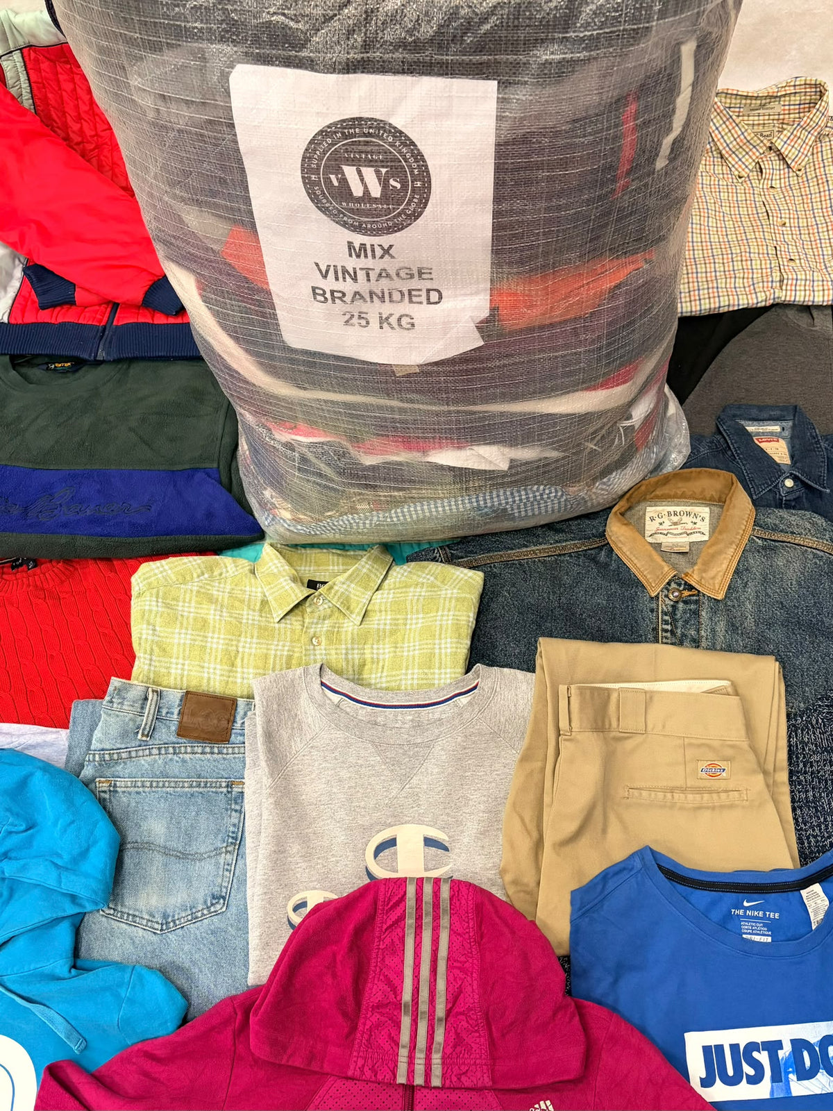 Clear sack labeled 25 kg of mixed vintage branded clothing above a colorful assortment of garments.