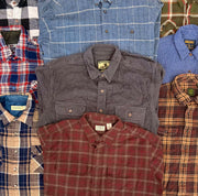 Assorted vintage flannel shirts in plaid and solid patterns, including blue, red, brown, and gray button-ups.