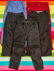 Three pairs of black and blue ski pants with reinforced knees, arranged on a colorful striped surface.