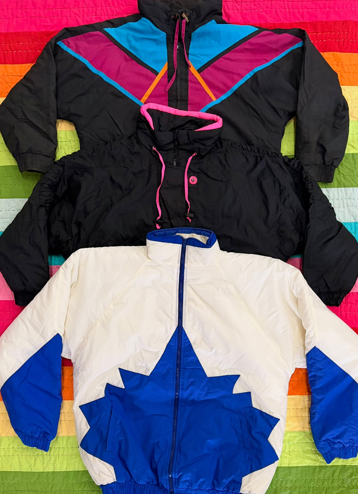 Two colorful vintage ski jackets, one black with neon trim and one white with blue and orange panels.