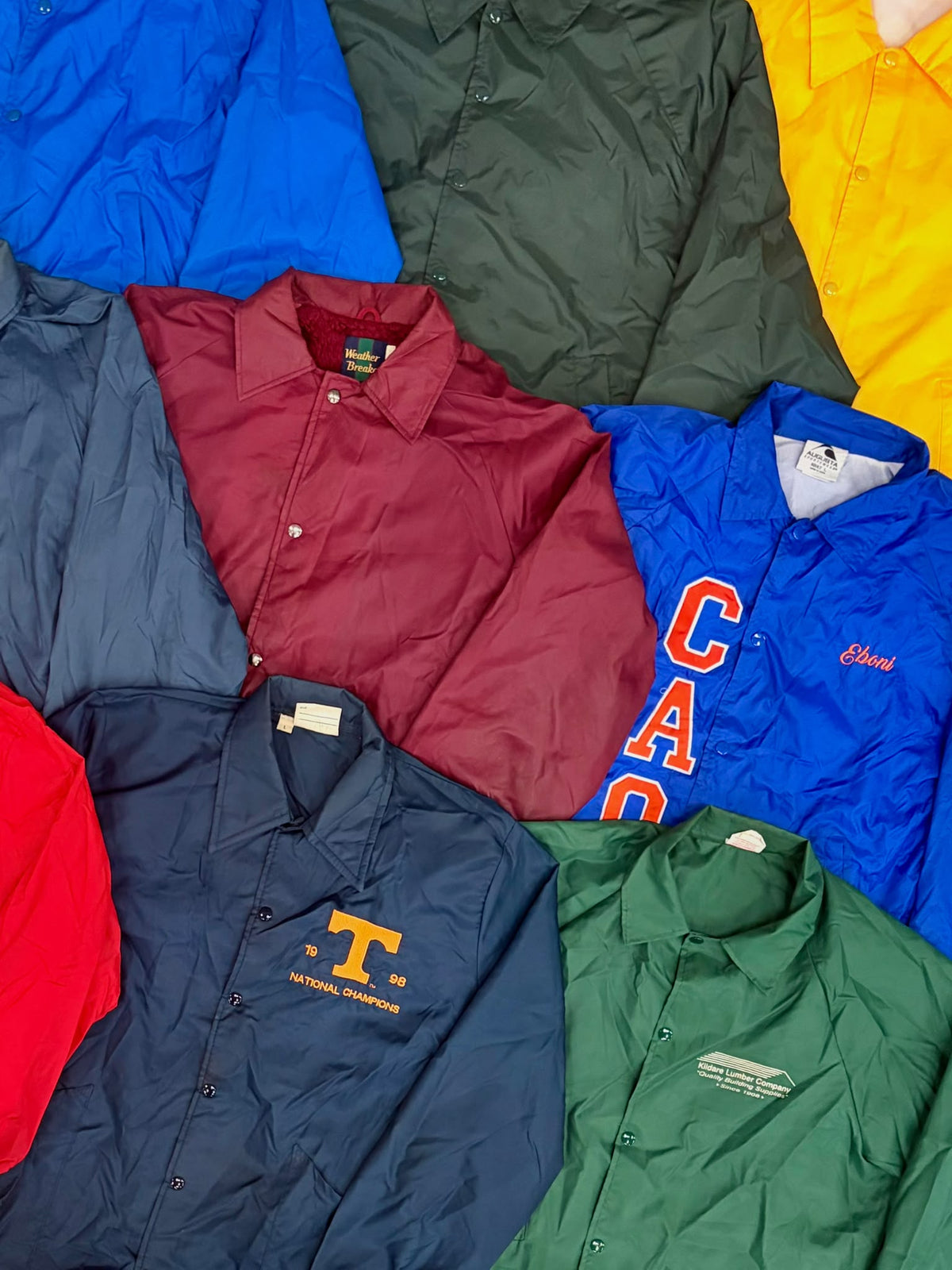 Assorted coach jackets in blue, burgundy, green, and navy, with snap fronts and collegiate logos.