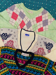 Stack of colorful patterned knit sweaters, including argyle, floral, and geometric designs in assorted colors.