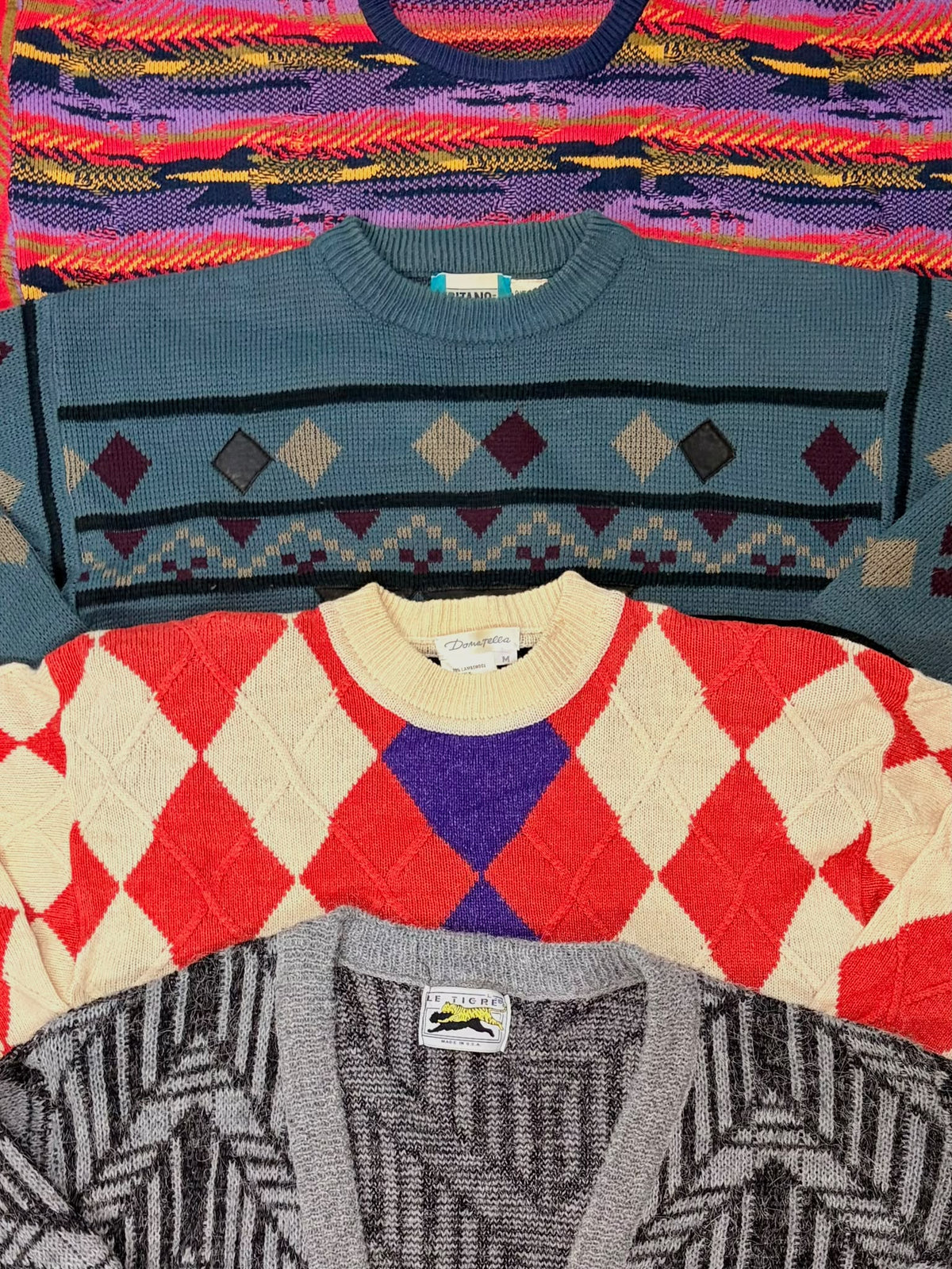 Three folded women’s patterned knit sweaters in teal, red and cream, and gray geometric designs.
