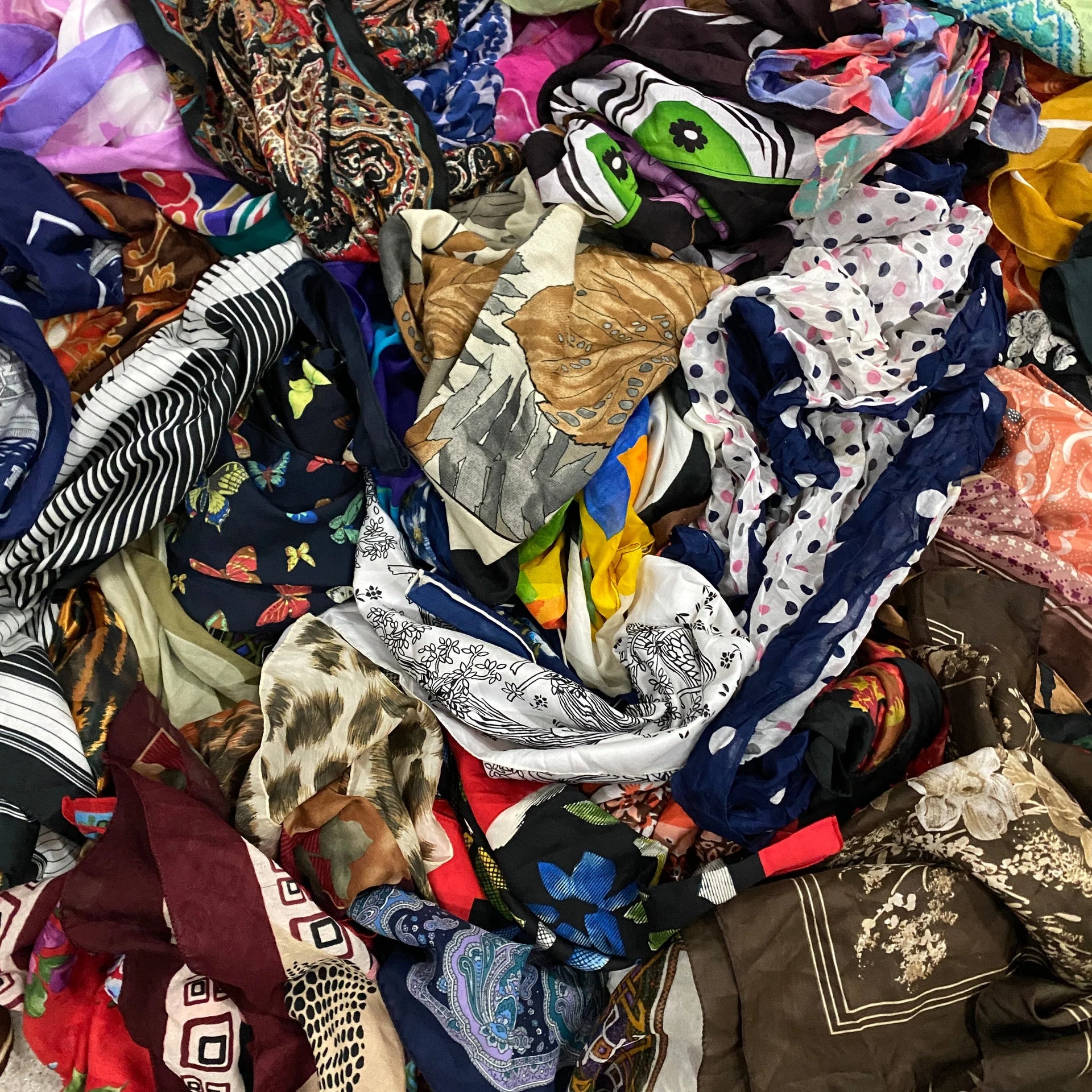 Mixed assortment of colorful patterned scarves including floral, animal print, stripes, and paisley designs.