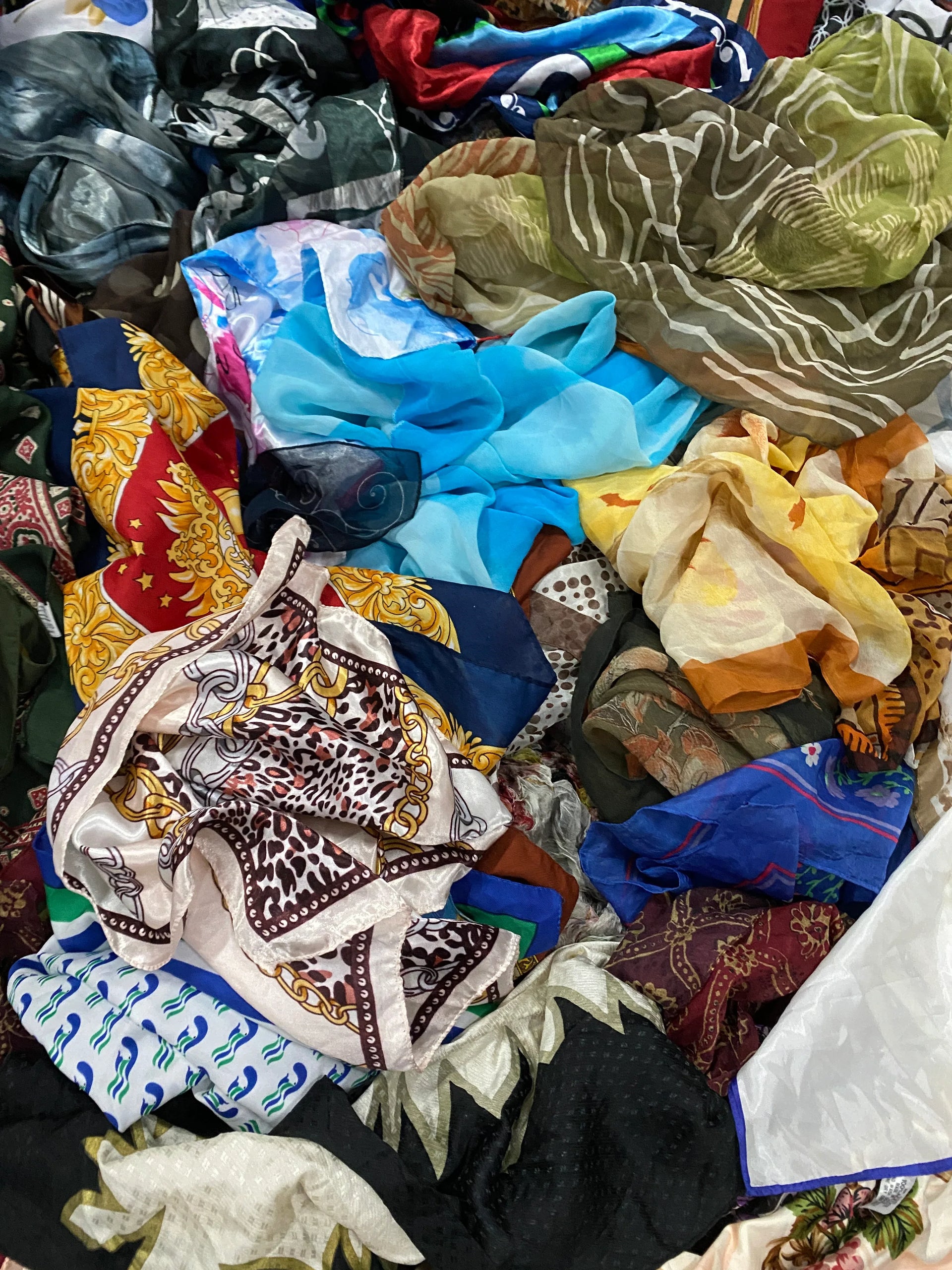 Pile of assorted colorful scarves in various patterns and fabrics, including floral, abstract, and geometric designs.